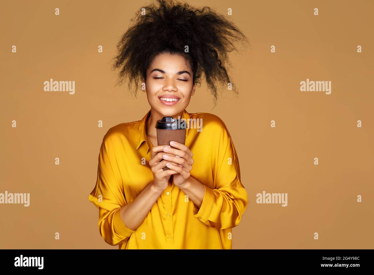 Young girl holds paper cup with hot coffee, takeaway. Photo of african american girl on beige background Stock Photo