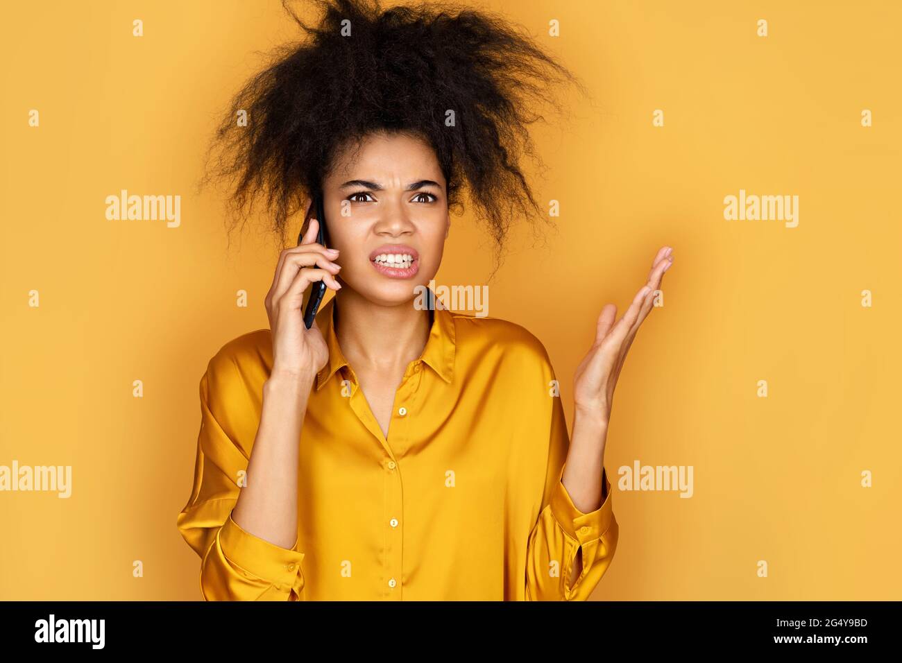 Angry girl talk on smartphone arguing or solving problem. Photo of african american girl on yellow background Stock Photo