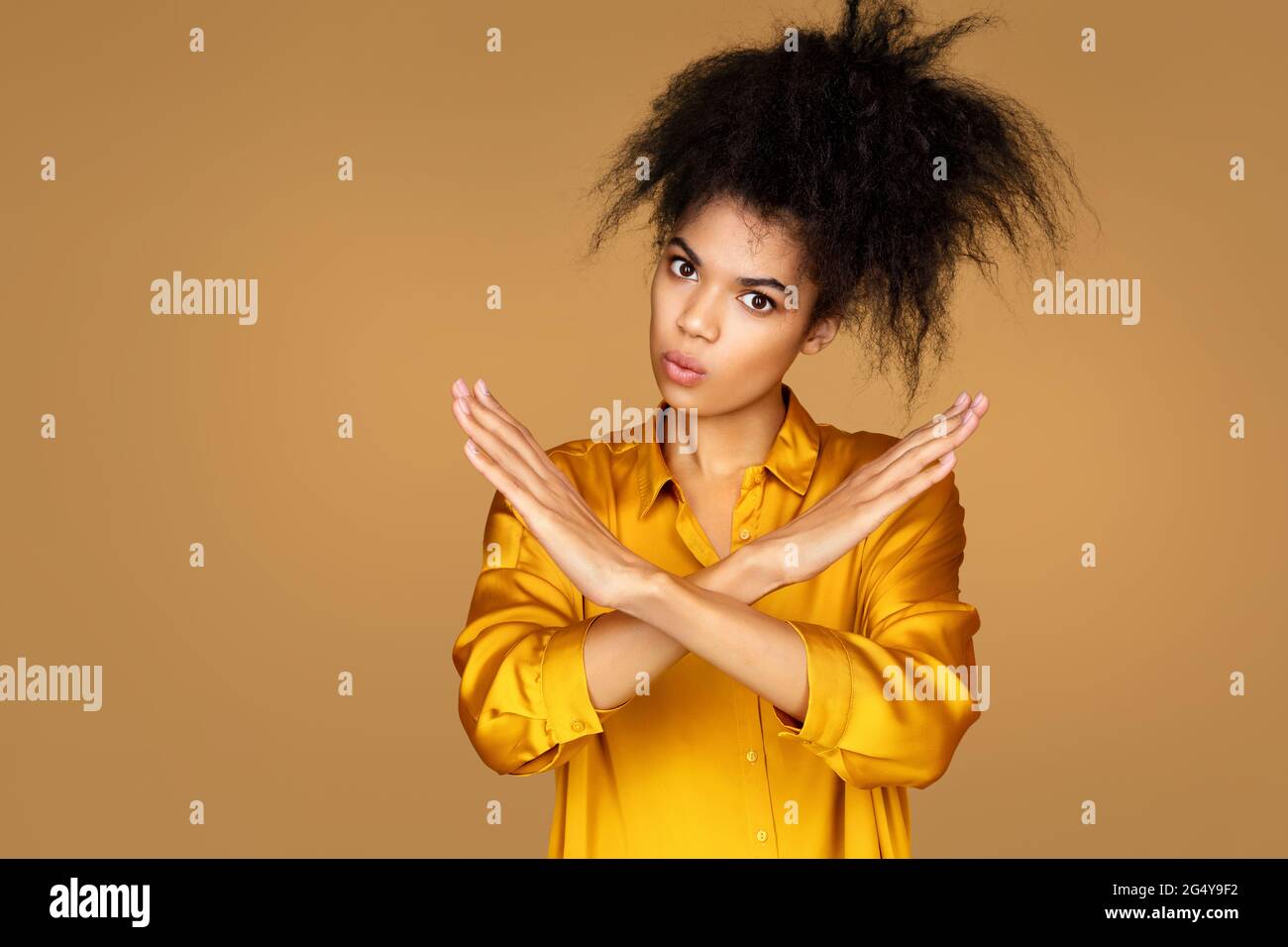 Girl raises arms in no or stop gesture. Photo of african american girl on beige background Stock Photo