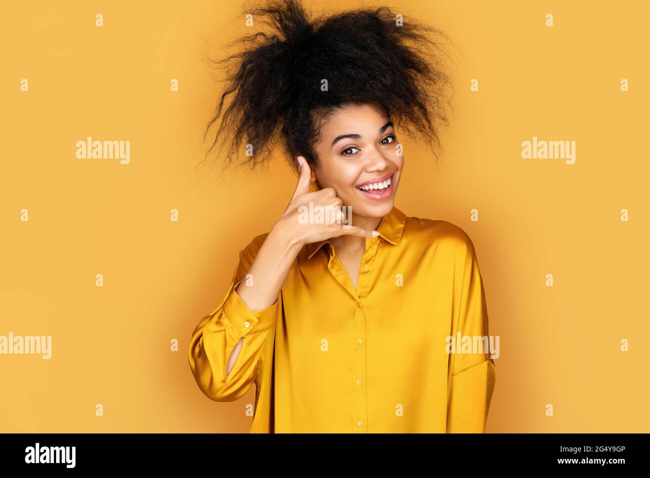 Smiling girl makes phone gesture of calling, call me back sign. Photo of african american girl on yellow background Stock Photo