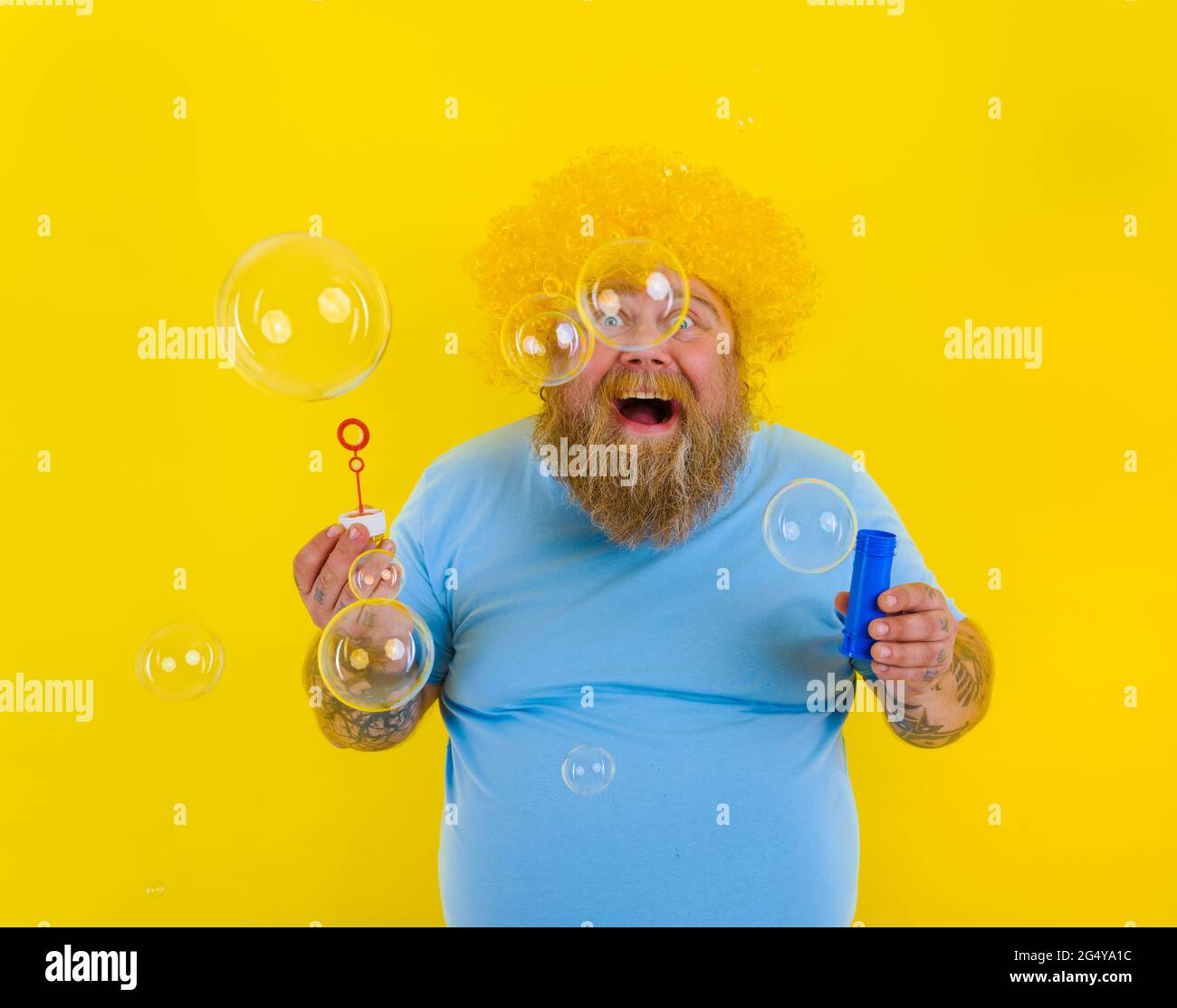 Amazed man with yellow wig in head play with bubbles soap Stock Photo