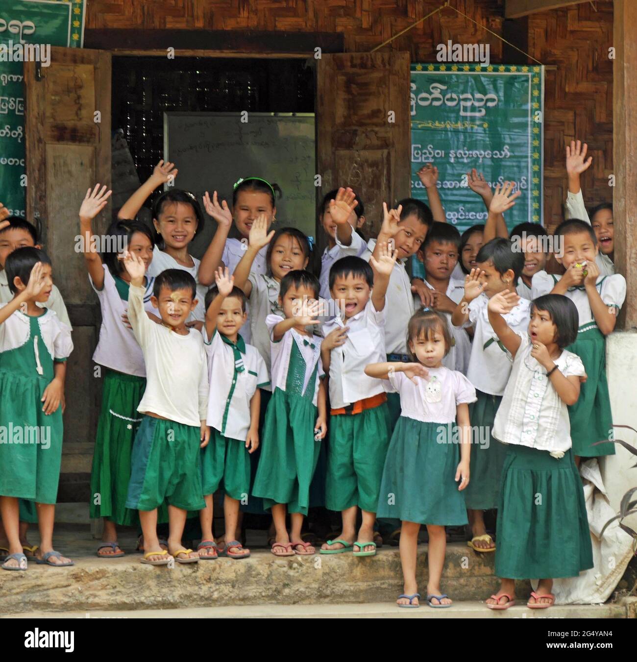 Group of young Myanmar schoolchildren in uniform waving and smiling