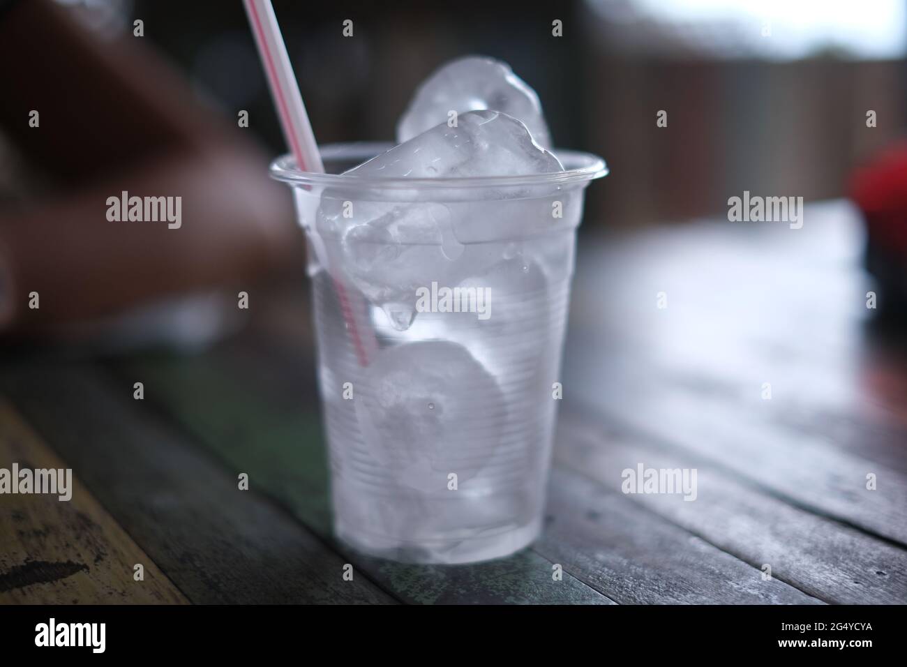 https://c8.alamy.com/comp/2G4YCYA/a-plastic-cup-with-a-straw-full-of-ice-cubes-on-a-wooden-table-2G4YCYA.jpg