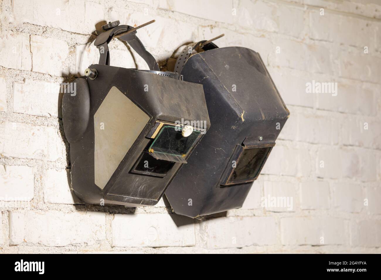 On a white wall hangs two welding masks Stock Photo