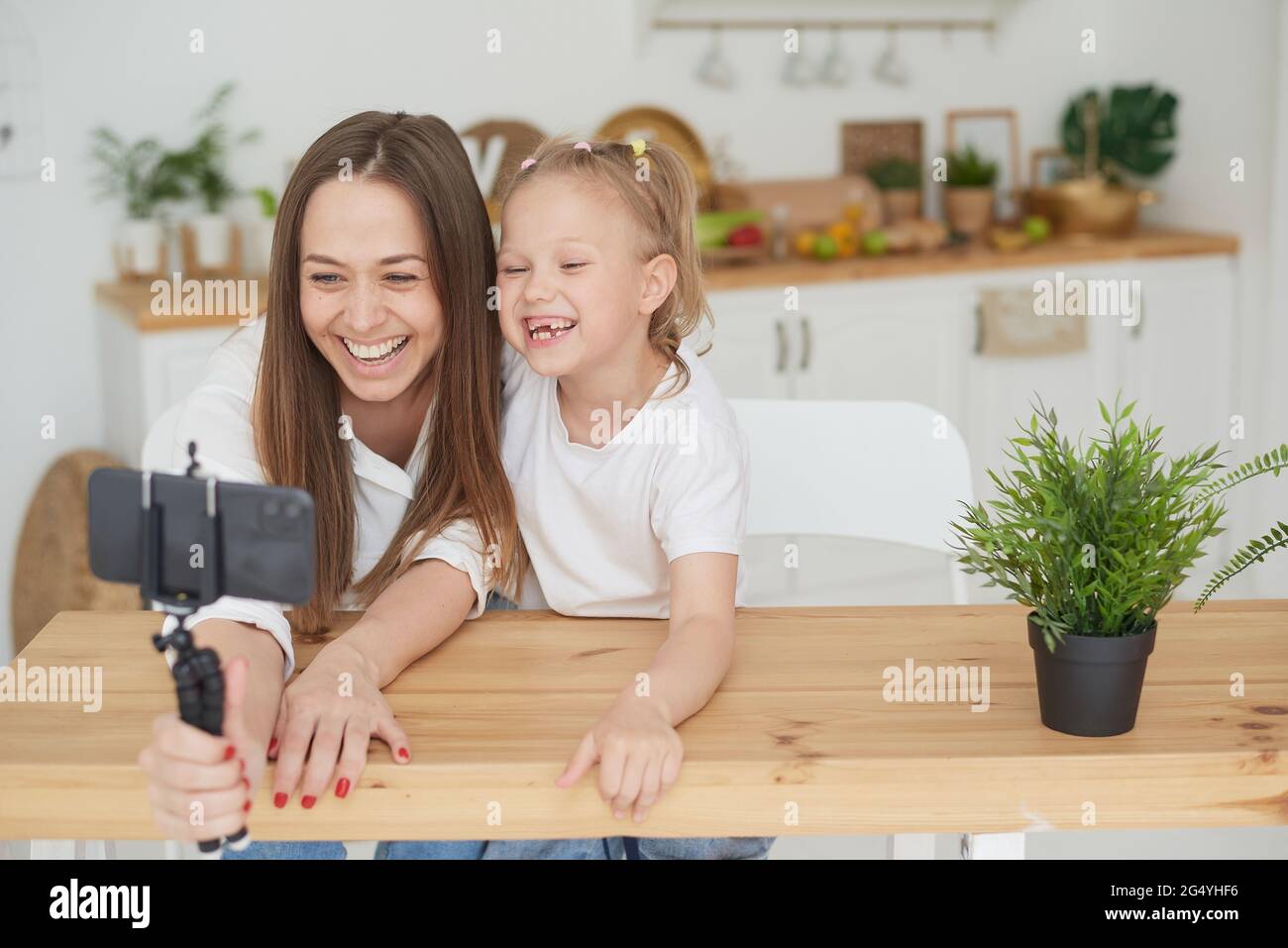 A happy family. Cute little daughter is sitting next to mom in the kitchen, laughing, having fun using a smartphone, watching a funny video. Video com Stock Photo - Alamy A happy family. Cute little daughter is sitting next to mom in the kitchen, laughing, having fun using a smartphone, watching a funny video. Video com Stock Photo - Alamy