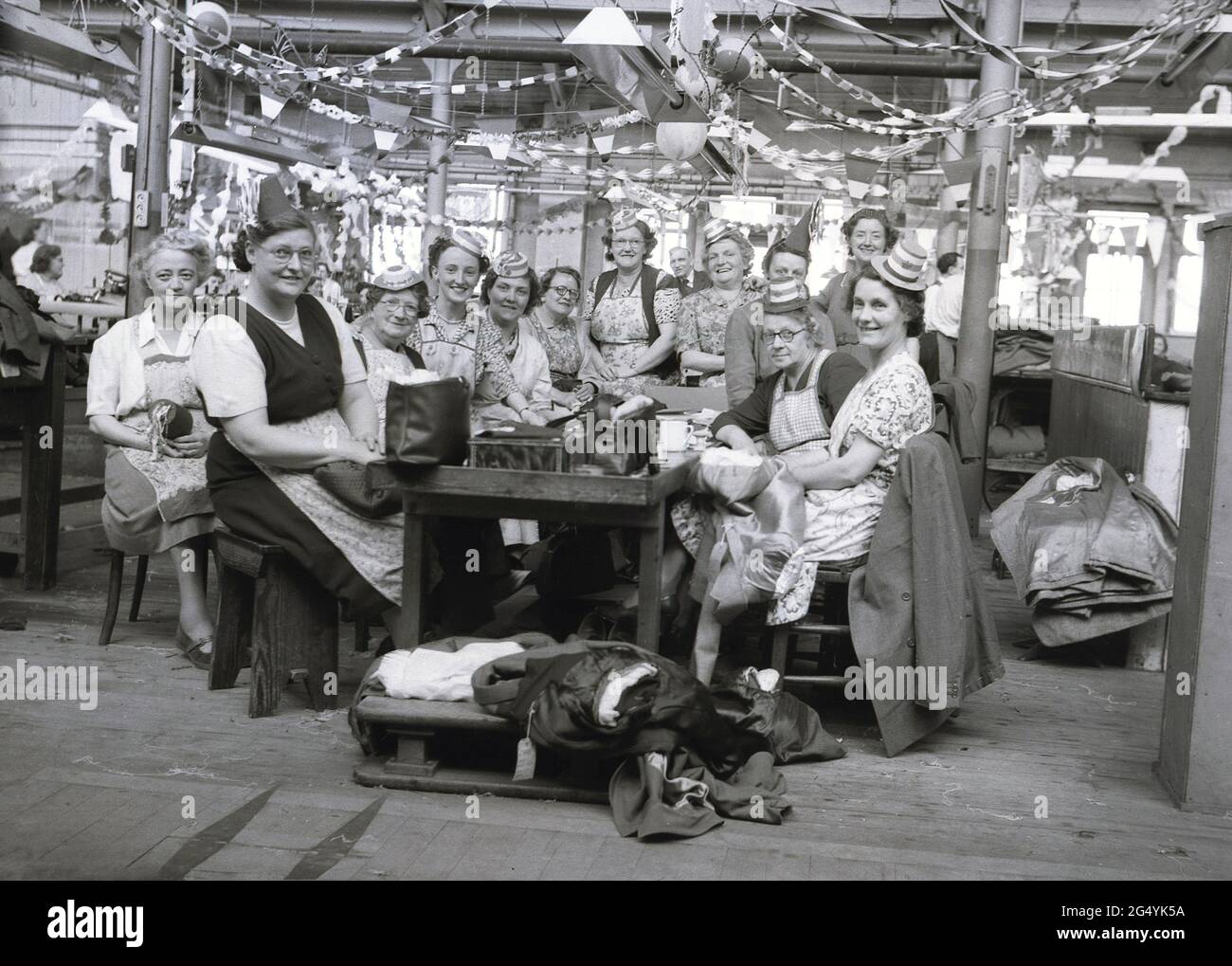 1957, historical, female workers in their pinafores and party hats sitting for a group photo at the Hepworths clothing factory, at Claypit Lane, Leeds, England, UK, as they celebrate the coronation of Elizabeth II to the throne. Stock Photo