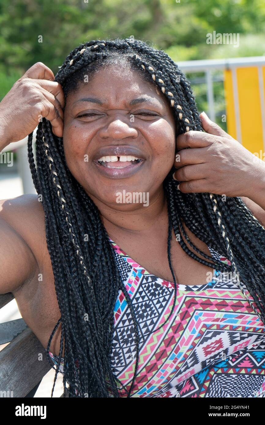 Posed portrait of a cheerful laughing attractive Nigerian American woman with long hair extensions. In Brighton Beach, Brooklyn, New York City. Stock Photo