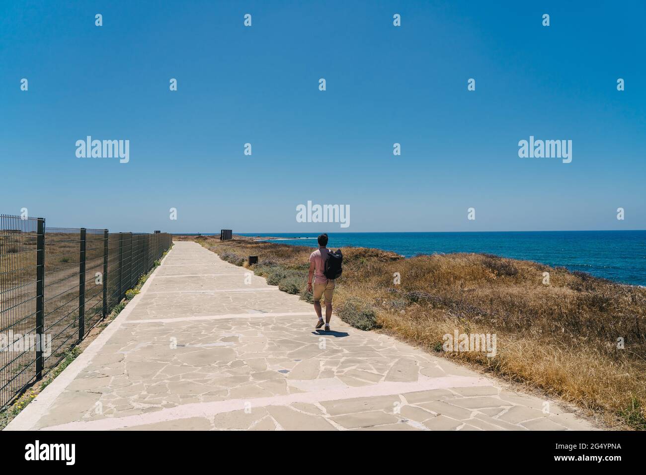 Theme of exploring island of Cyprus on foot. Man with a backpack is walks along the sea by coastal broadwalk in the city of Paphos on Cyprus in summer Stock Photo