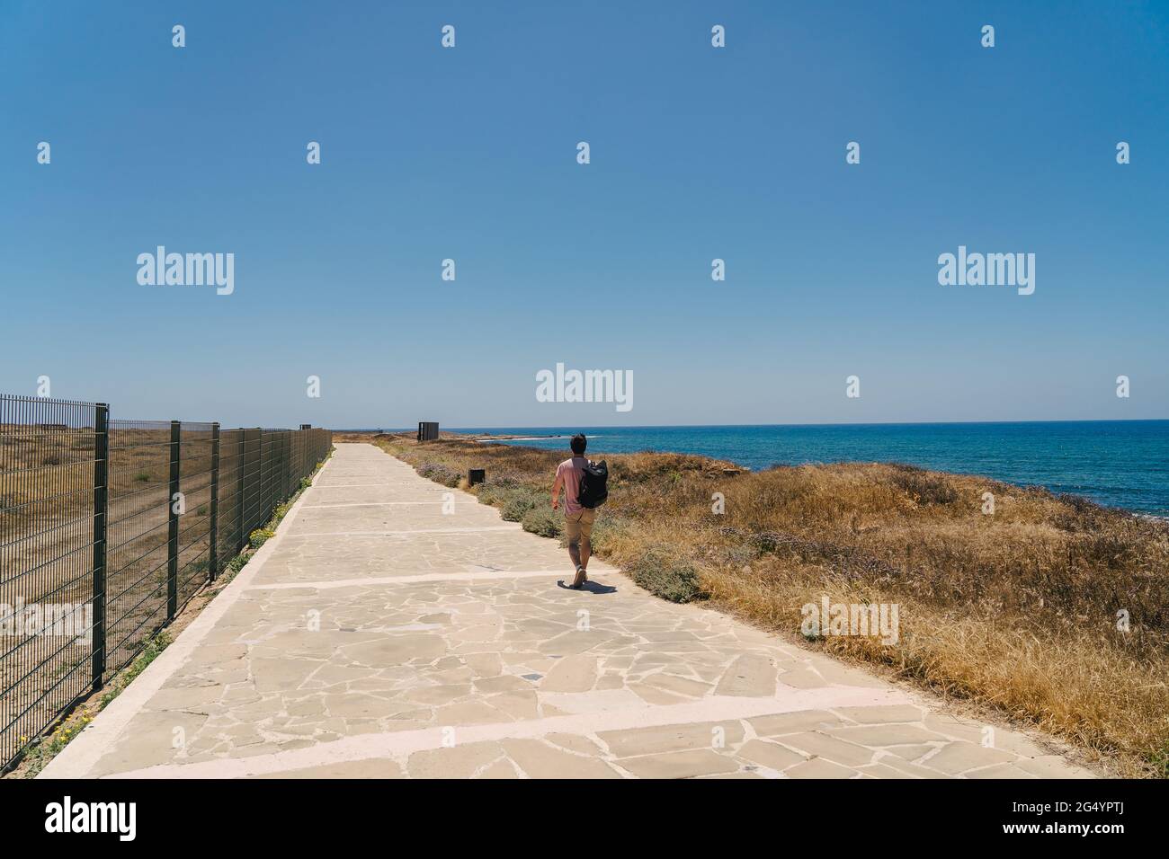 Coastal broadwalk along mediterranean sea on island of cyprus in city of paphos. Traveler with backpack walks along walking path near seafront. Active Stock Photo