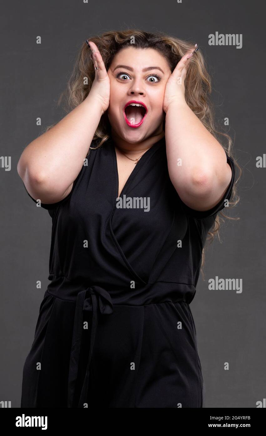A beautiful fat woman with long curly hair screams loudly. A plump girl with an emotion of indignation and horror. Stock Photo