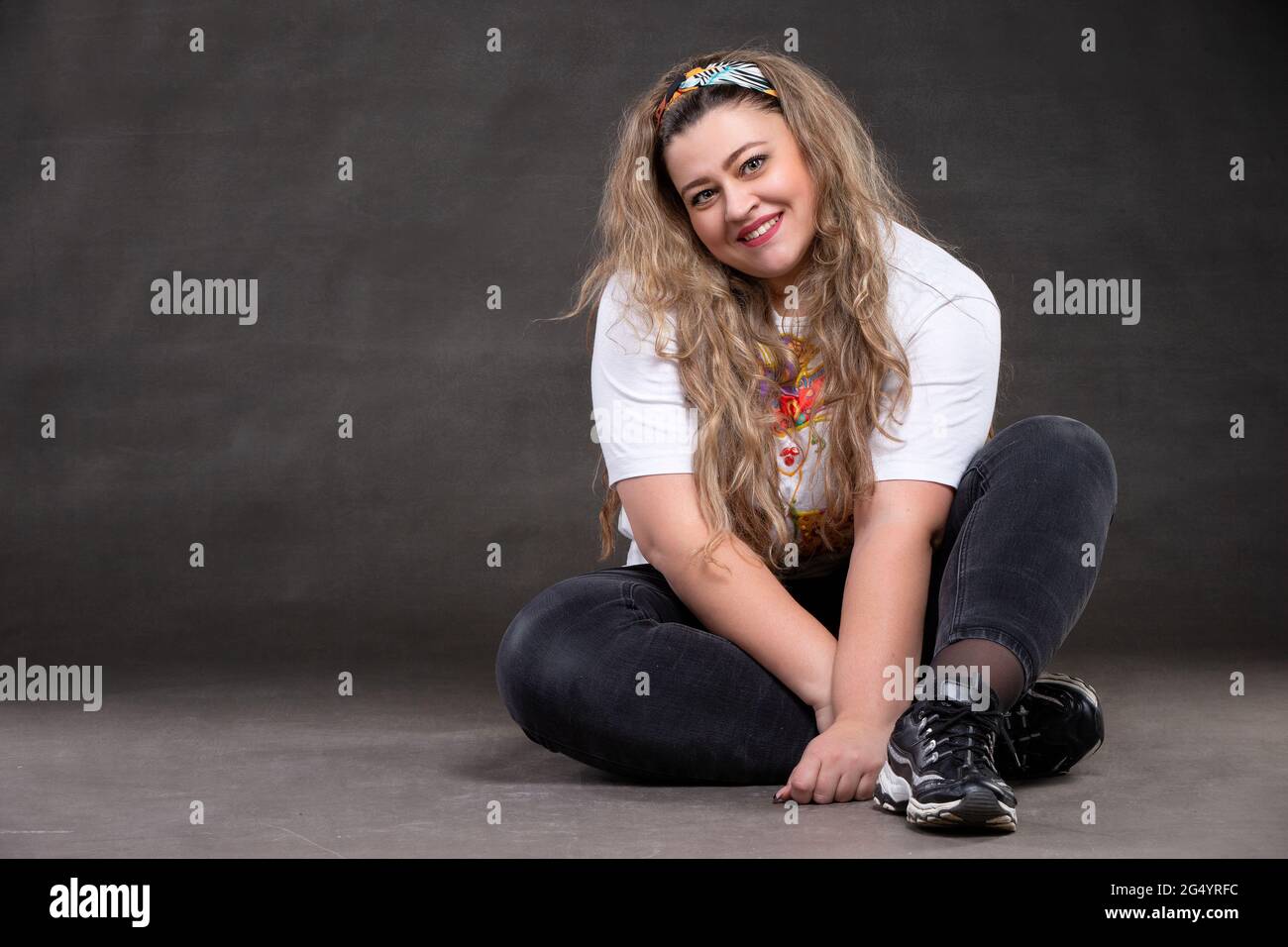 Beautiful fat woman on a gray background looks at the camera and smiles. The girl is a plus size model. Stock Photo