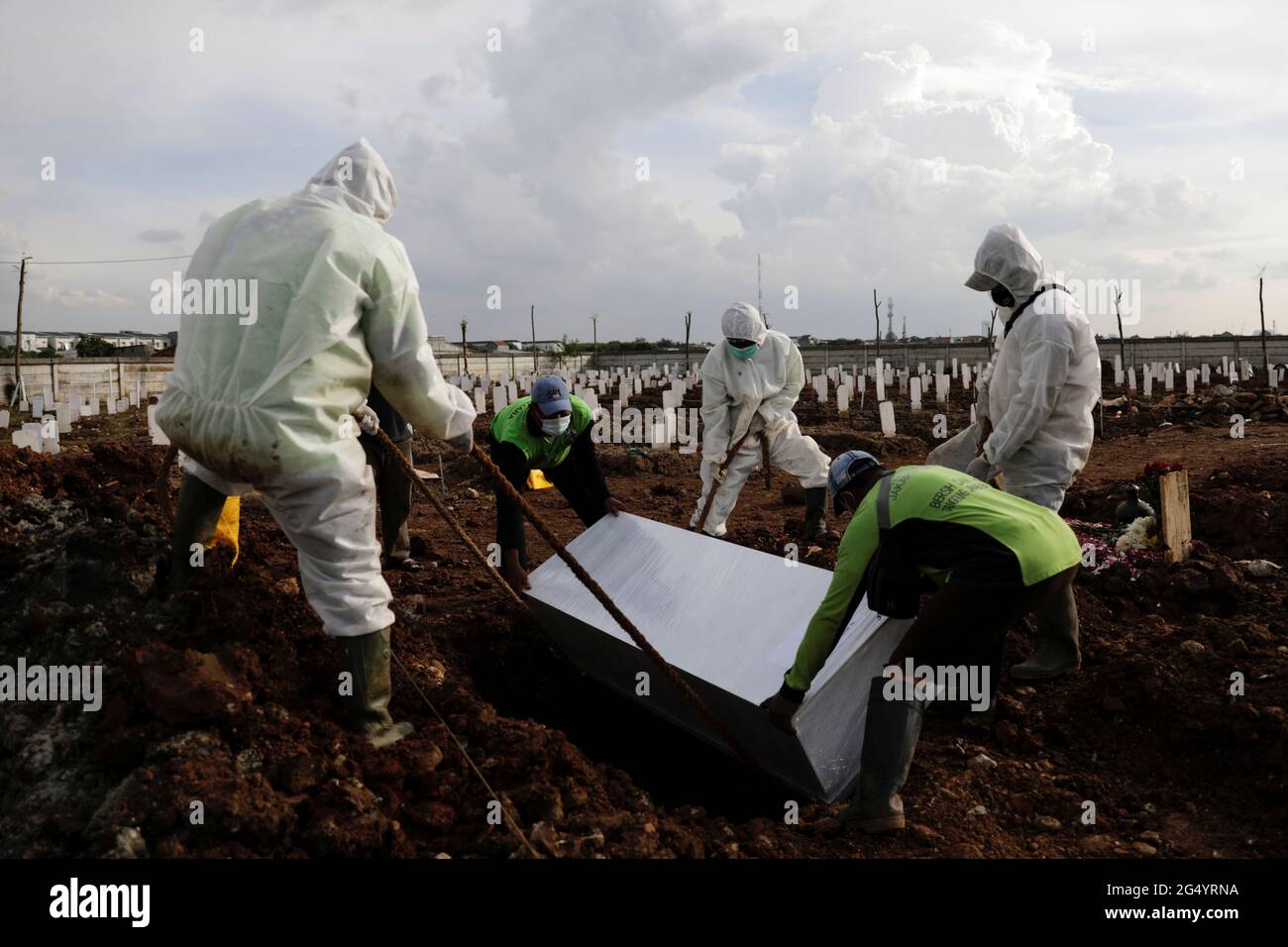 Municipality workers wearing personal protective equipment (PPE) burry a coffin of a coronavirus disease (COVID-19) victime at the burial area provided by the government for victims of the coronavirus disease (COVID-19) in Jakarta, Indonesia, June 24, 2021.REUTERS/Willy Kurniawan Stock Photo