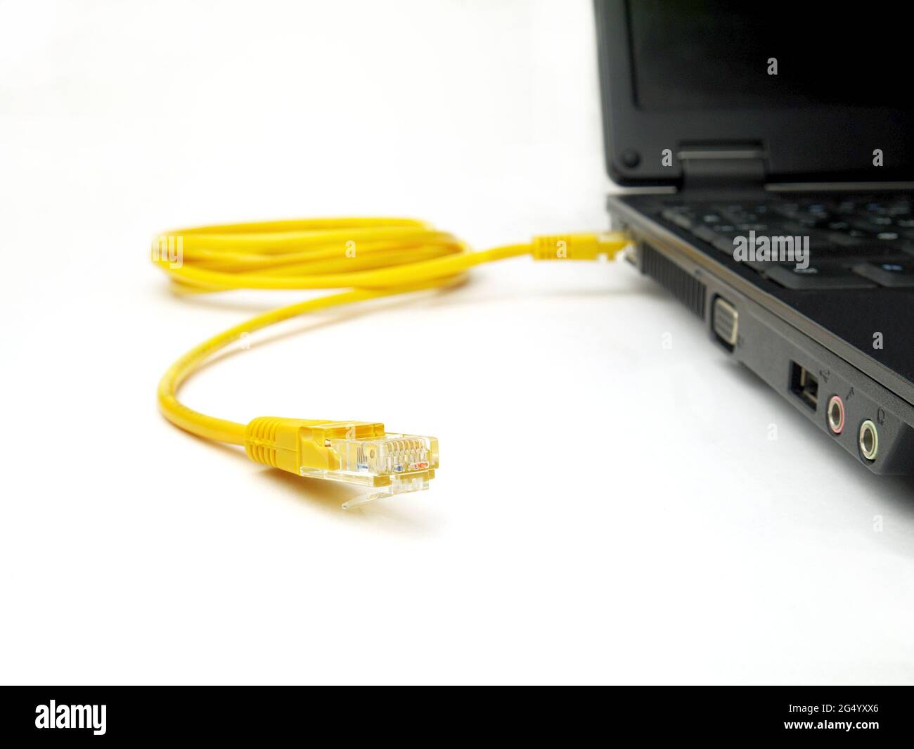 yellow twisted pair ethernet network cable connected to laptop, closeup, white background, focus on unplugged network connector Stock Photo