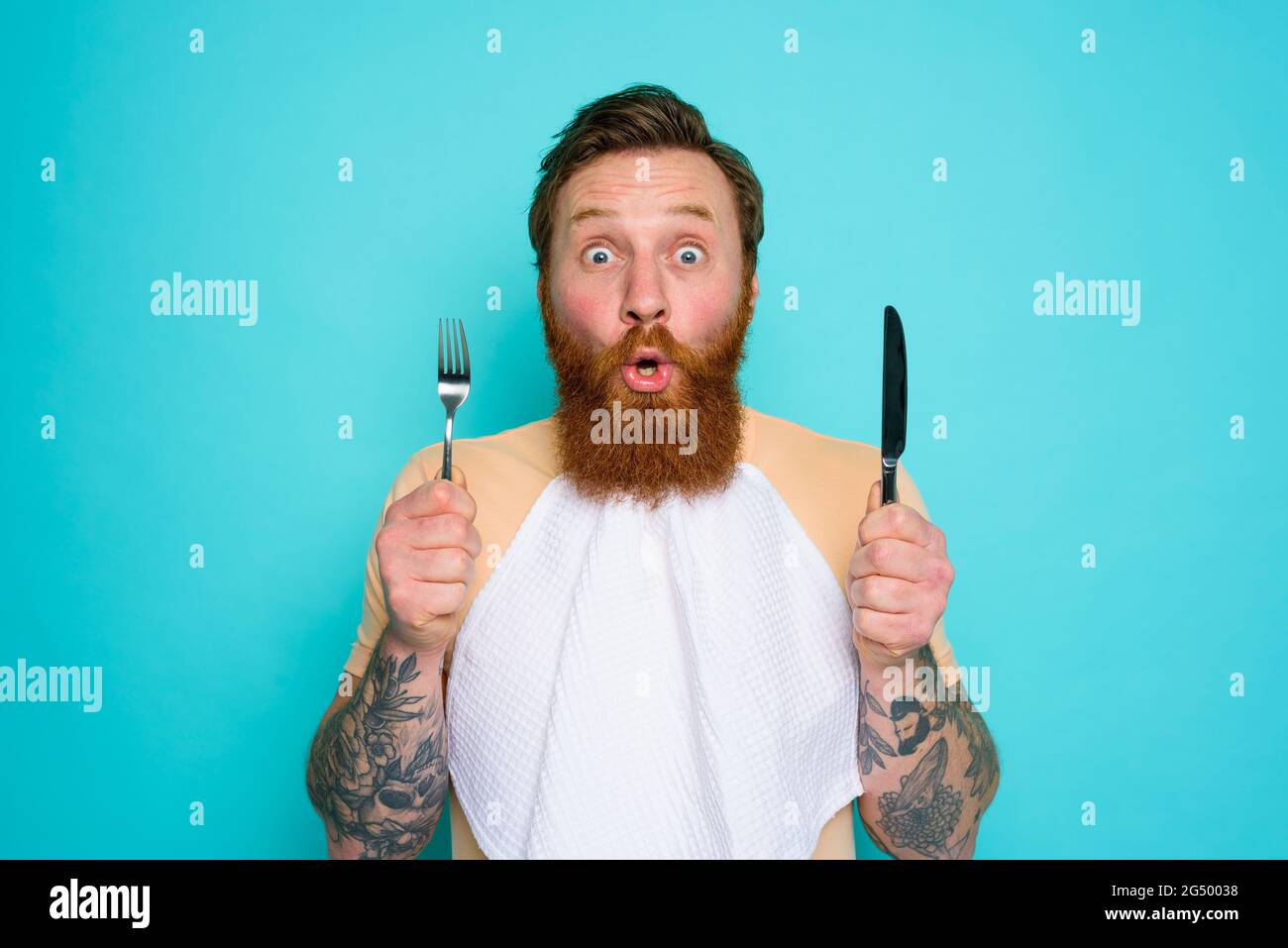 Shocked man with tattoos is ready to eat something with cutlery in hand Stock Photo