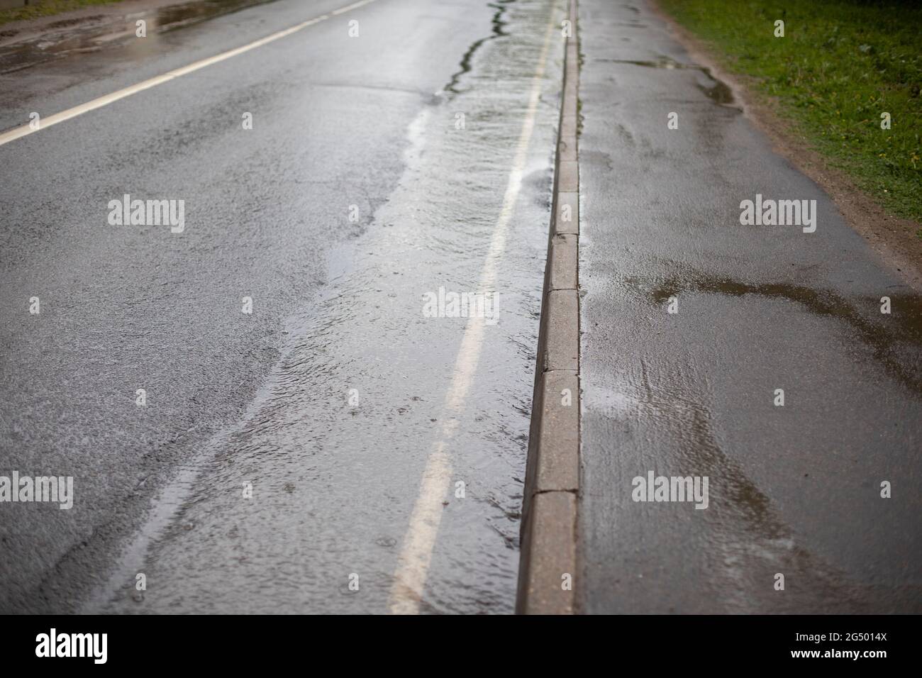 A meadow on a dart. The side of the road is flooded with rain. A lot of water flows along the road. Stock Photo