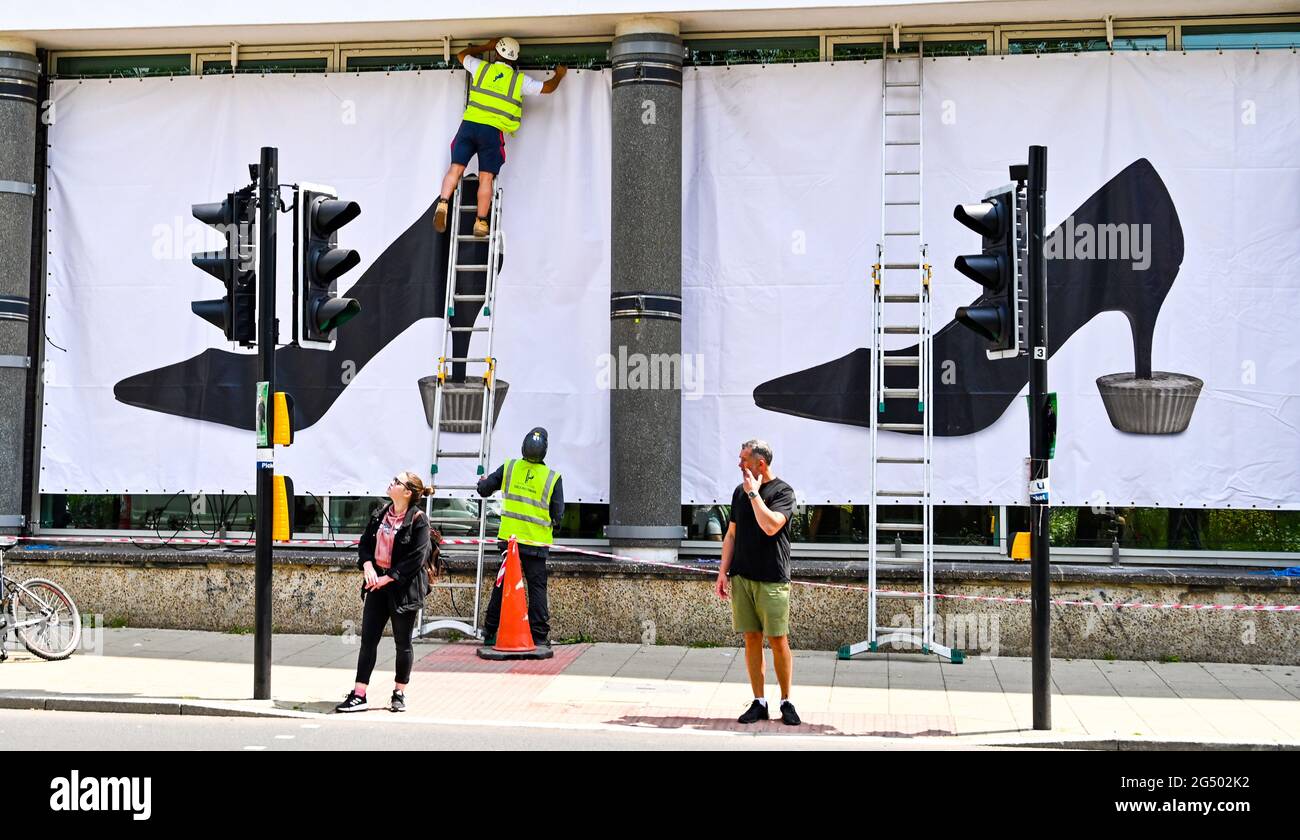 Brighton UK 24th June 2021 - Giant banners showing artist Alexandre da Cunha's iconic image of a woman’s black stiletto anchored within a concrete fairy cake are are put up at the Centre for Contemporary Arts in Brighton as part of this years summer commission .The summer commission is a series of public art works in Brighton and year a selected artist is chosen to create a new work for the front of the Brighton CCA galleries.: Credit Simon Dack / Alamy Live News Stock Photo