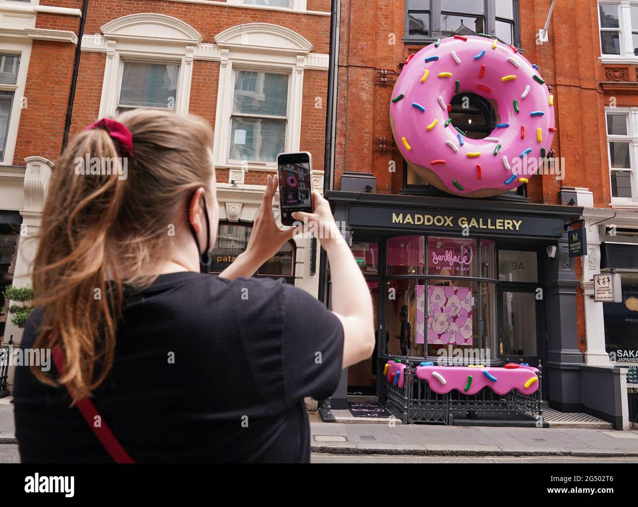 A woman takes a photo of a giant donut installation outside the Maddox Gallery in Mayfair, London, to celebrate a new exhibition entitled Villainy, a body of work by an anonymous street artist from New York who operates under the alias, 'Jerkface'. Picture date: Thursday June 24, 2021. Stock Photo
