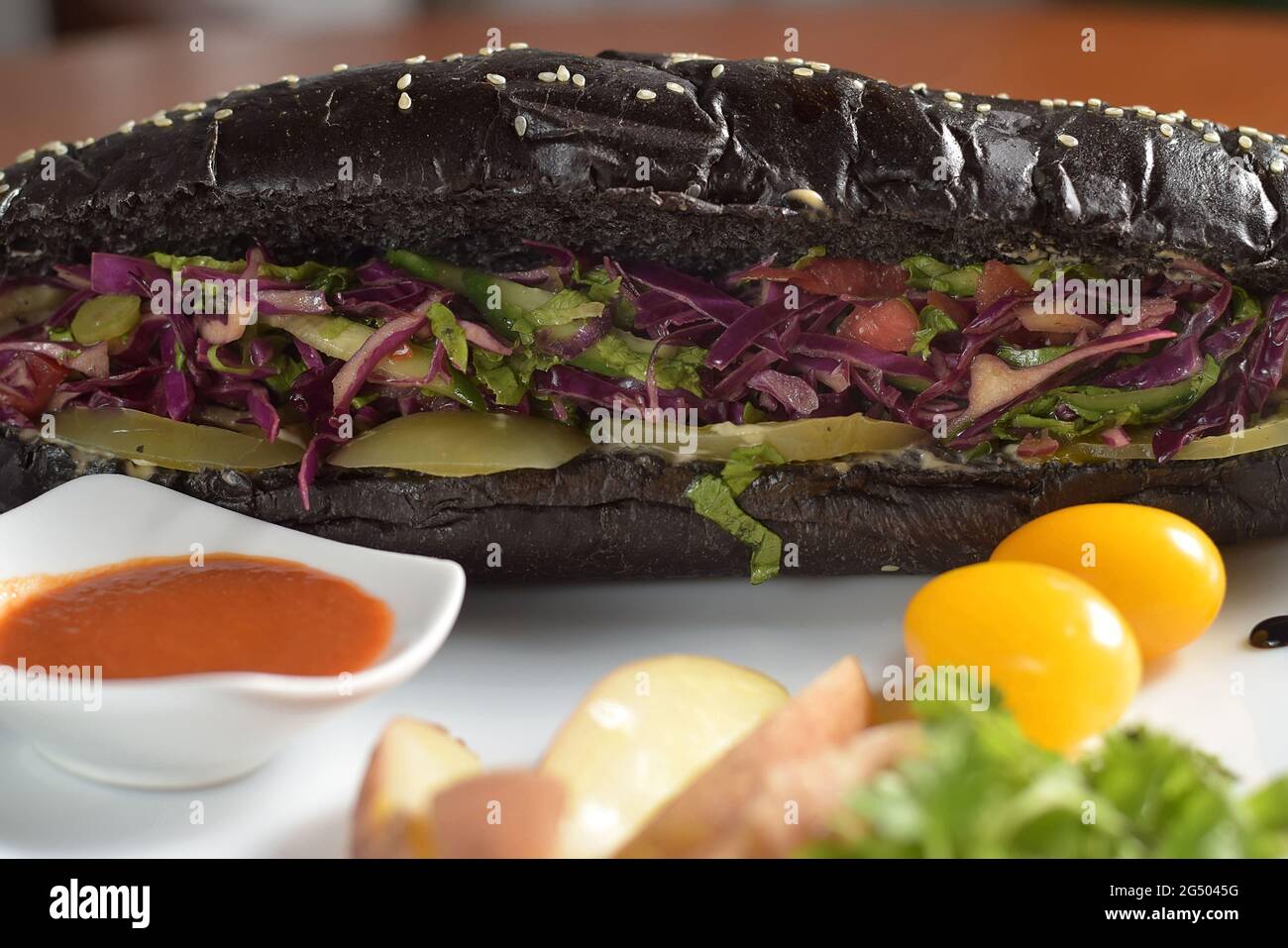 Long black hot dog with fried chicken sausage with salad, on a plate with sauce, tomatoes and potatoes,close-up Stock Photo