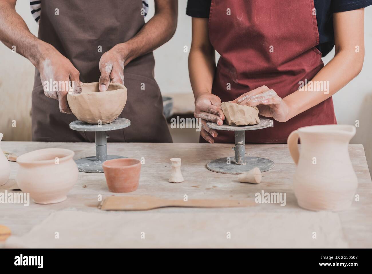 partial view of young african american couple in aprons making clay pots on table with equipment in pottery Stock Photo