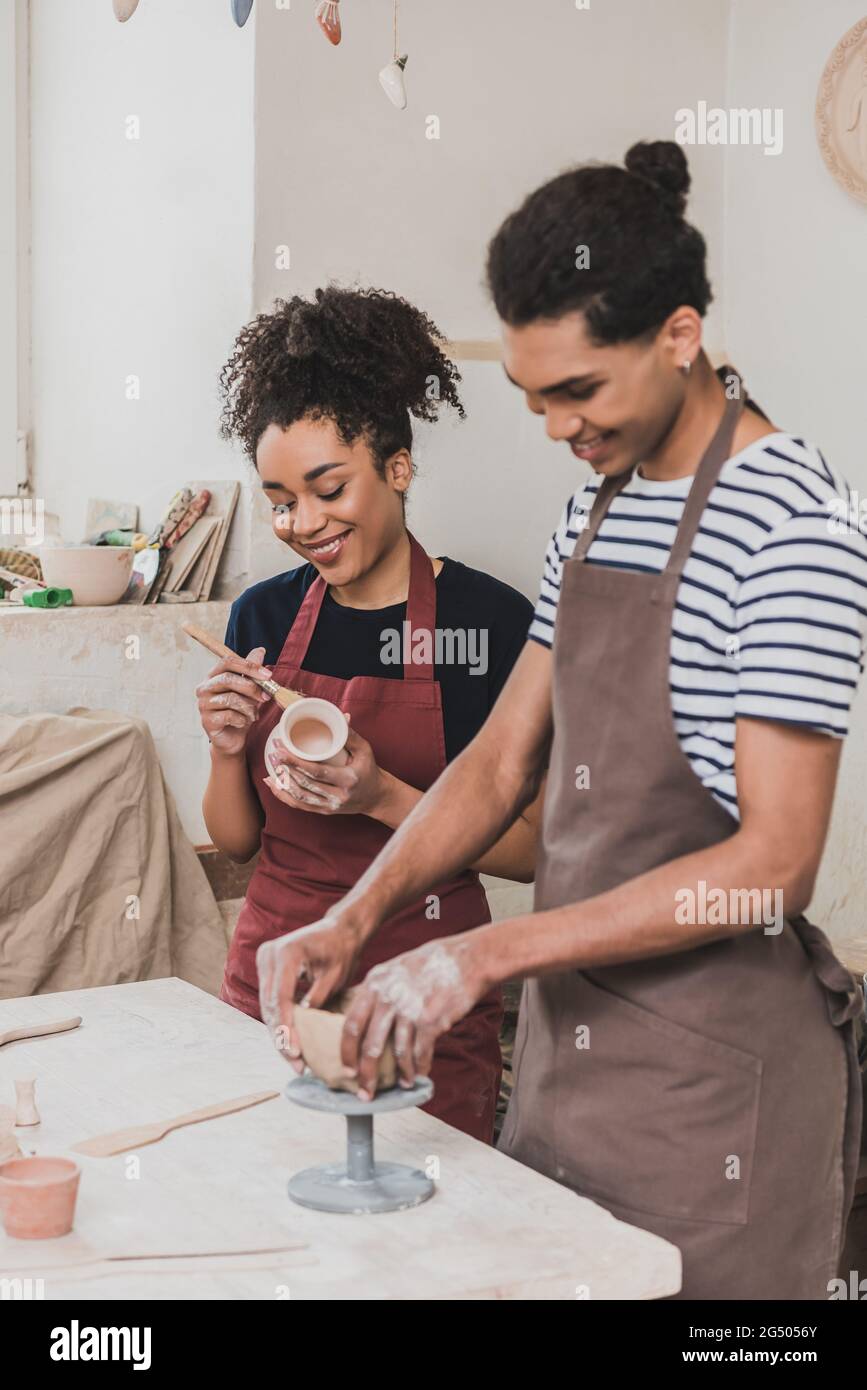 smiling young african american man and woman sculpting clay pot in ...