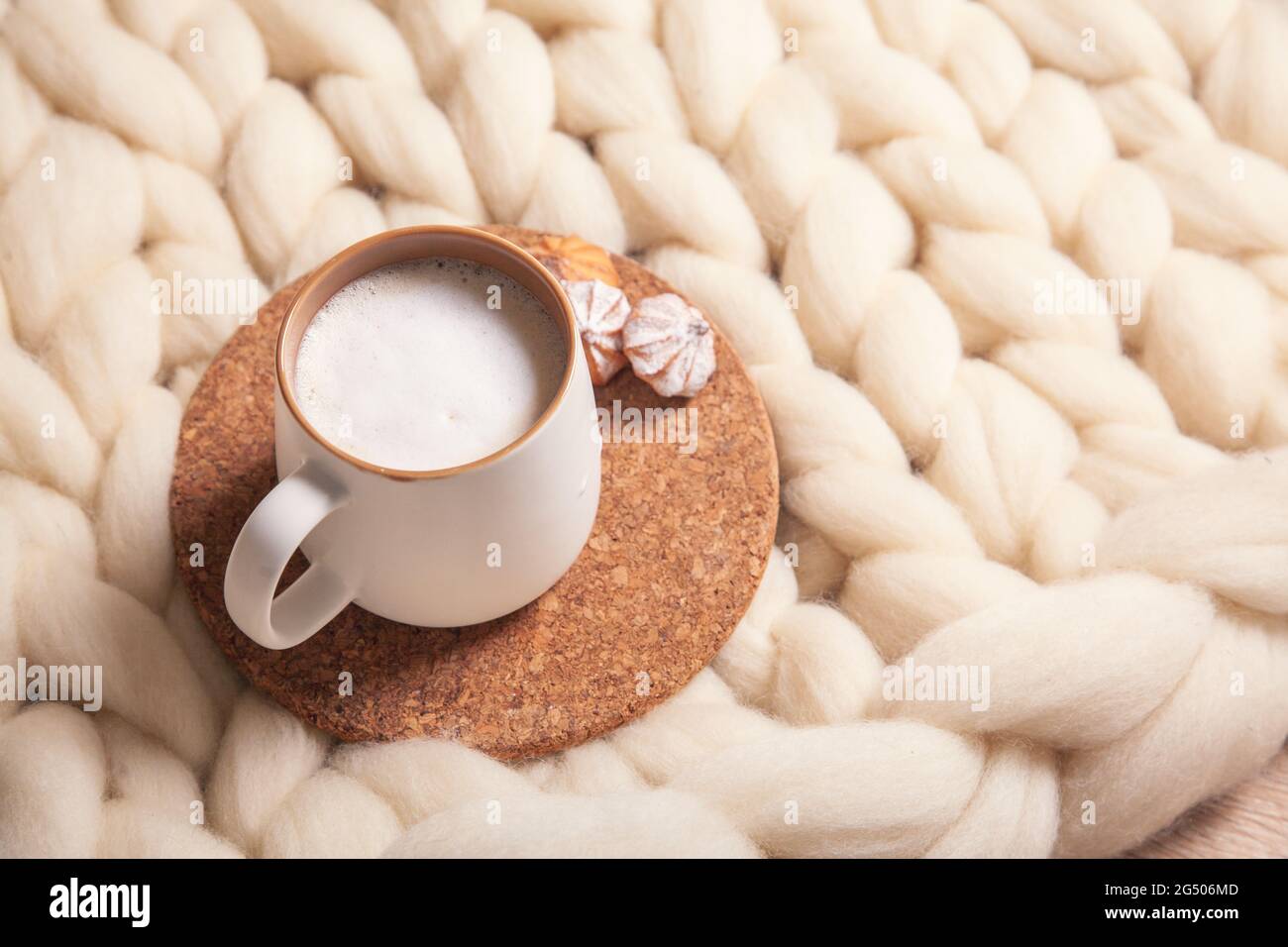 A cup of cappuccino and cookies on the background of a large-knit blanket. The atmosphere of homeliness and comfort. Stock Photo