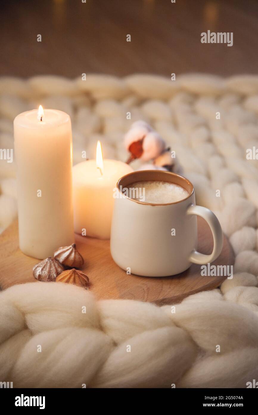 Cup of cappuccino, cookies, and candles on the background of blanket of thick yarn. The atmosphere of homeliness and comfort. Stock Photo