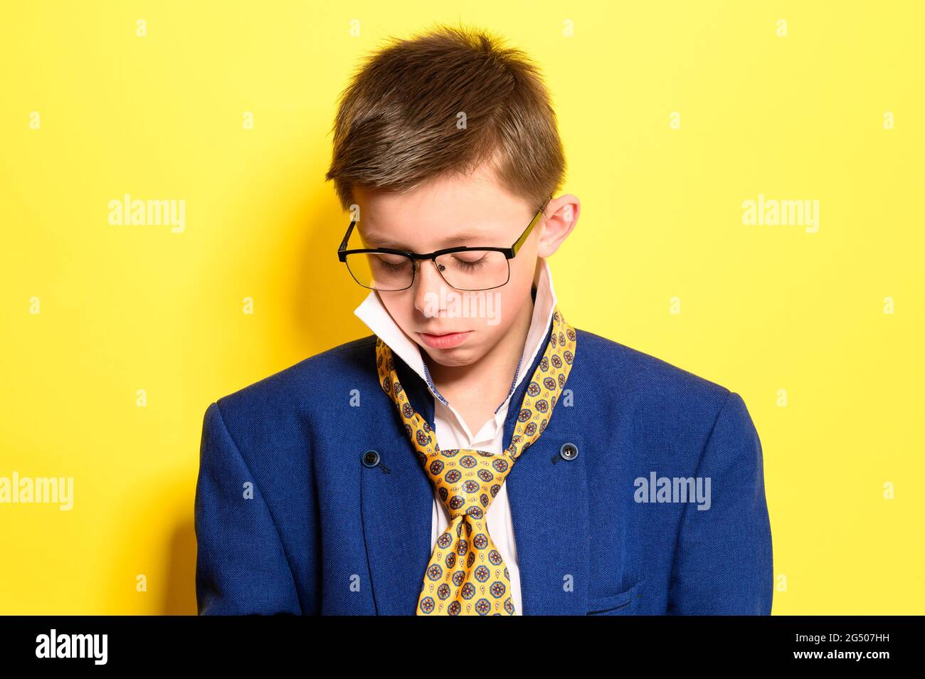 Portrait of a boy on a yellow background with a sad expression, an adult suit on a child. Stock Photo