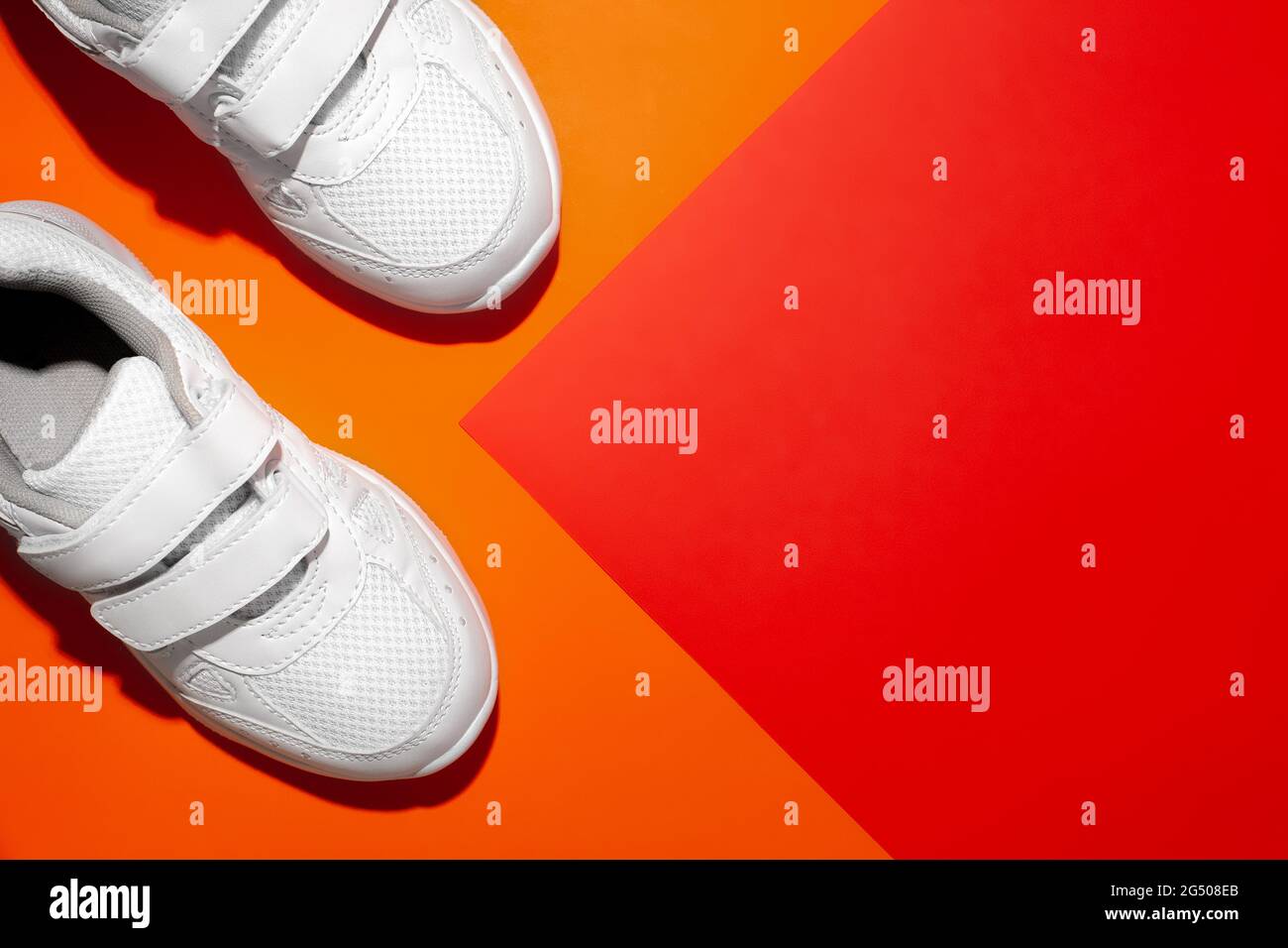 top view the front of two white sneakers with hard shadows on the side on a geometric paper orange and red background with copy space Stock Photo