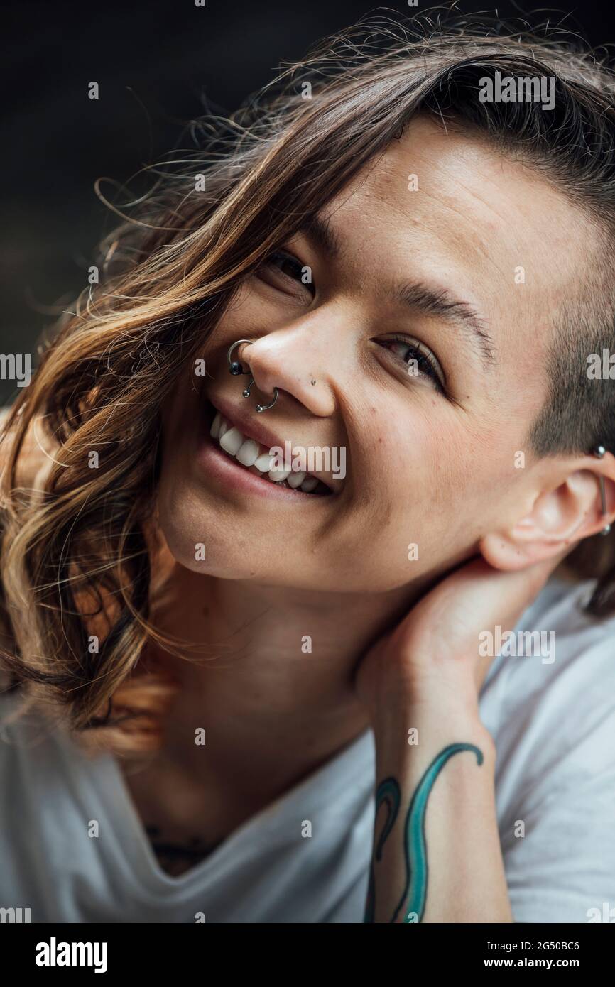 A portrait of a young woman smiling and leaning her head on her hand while looking at the camera. Stock Photo