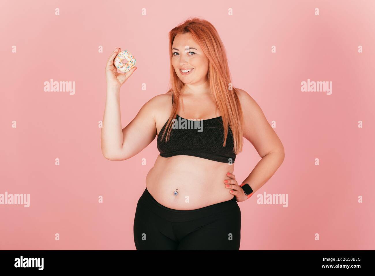 plump girls Smiling beautiful plump girl wearing sports outfit holding sweet donut  while standing on pink background Stock Photo - Alamy