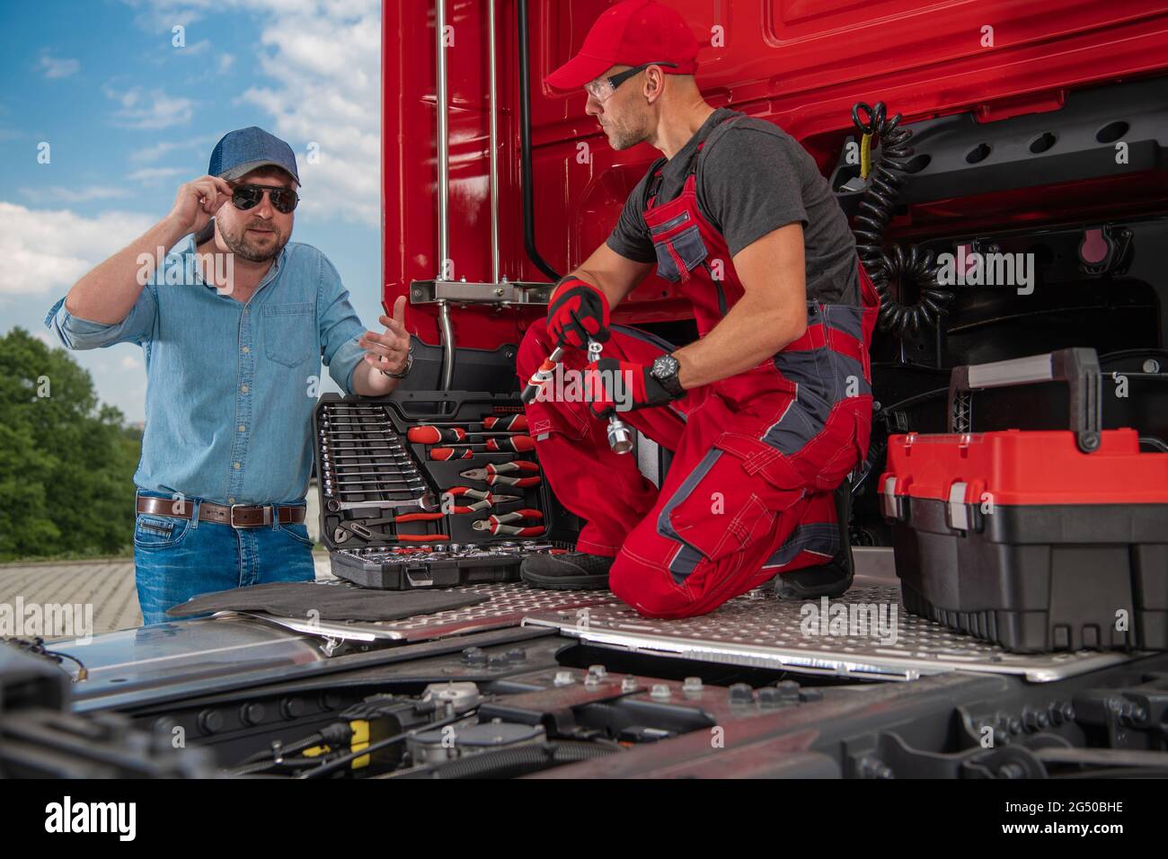 Trucker and Professional Truck Mechanic Making Conversation Regarding Semi Truck Technical Issue. Heavy Duty Transportation Theme. Stock Photo