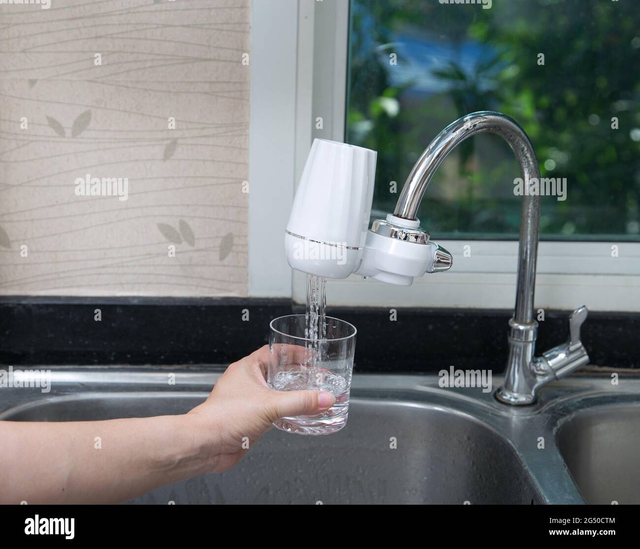 woman pouring water into glass from the water filter in the kitchen. Pouring clean fresh drink. Stock Photo