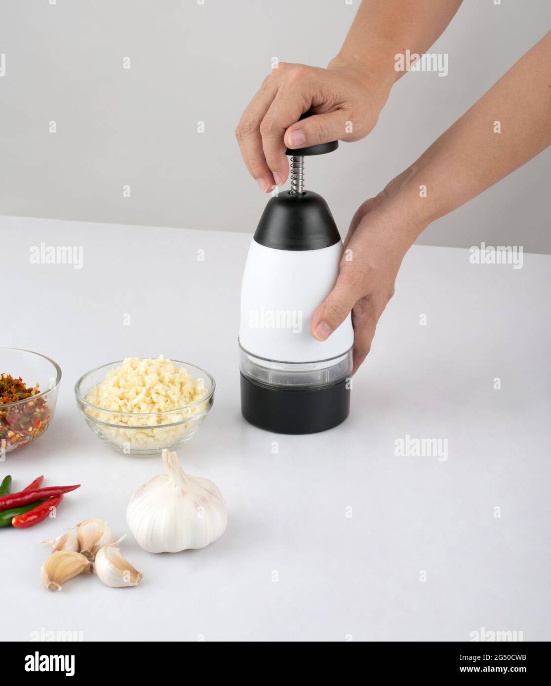 woman chopping garlic and chili with chopper tool on white table in the kitchen Stock Photo