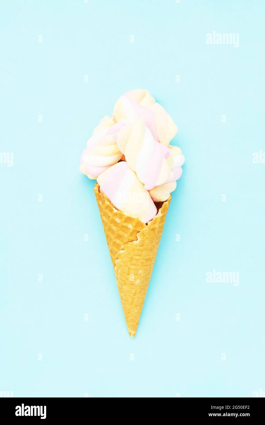 Colorful marshmallow candy in an ice cream cone on a blue background. Flat lay, copy space, vertical. Stock Photo