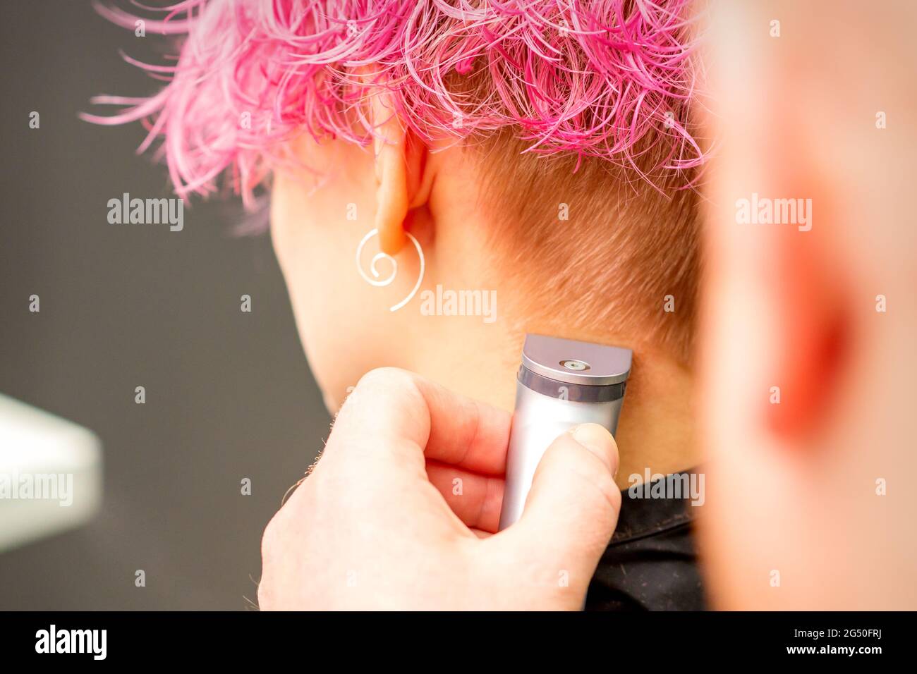 Back view of hairdresser's hand shaving nape and neck with electric trimmer of young caucasian