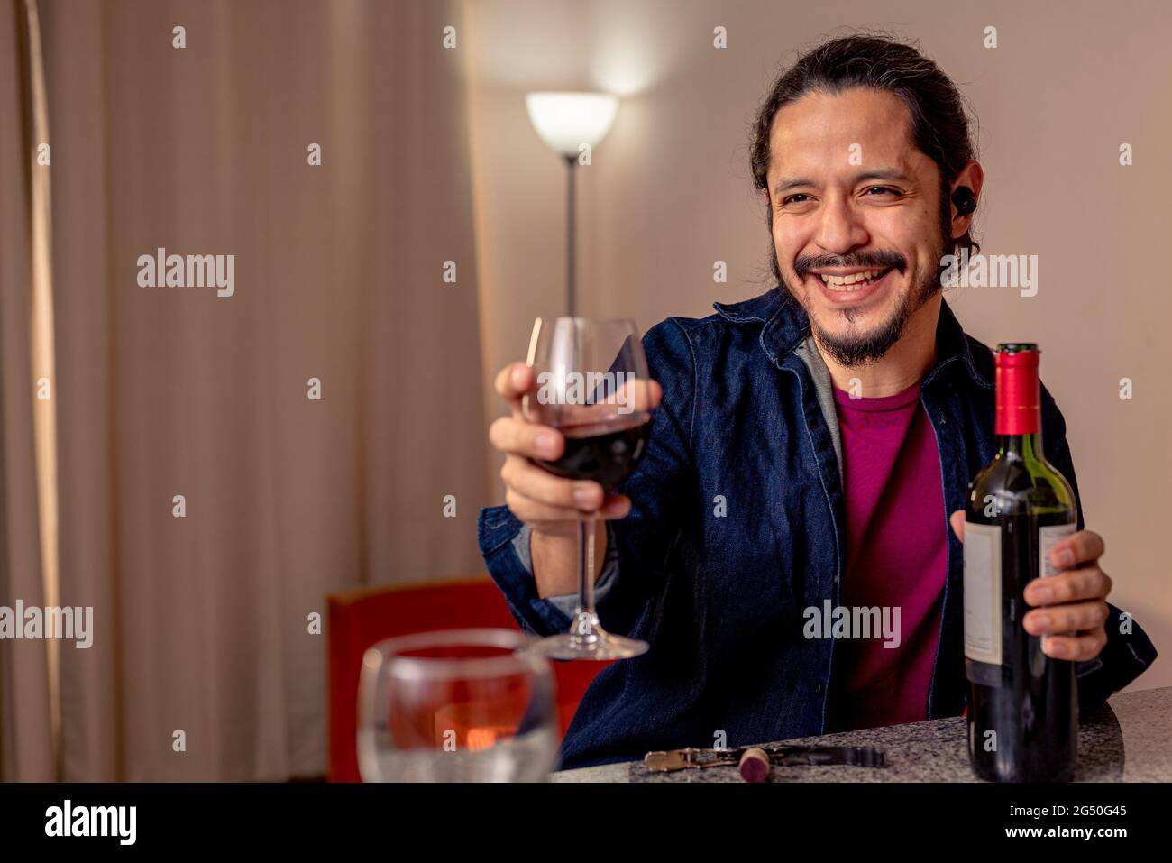 Young latin man drinking red wine at home in the living room Stock Photo