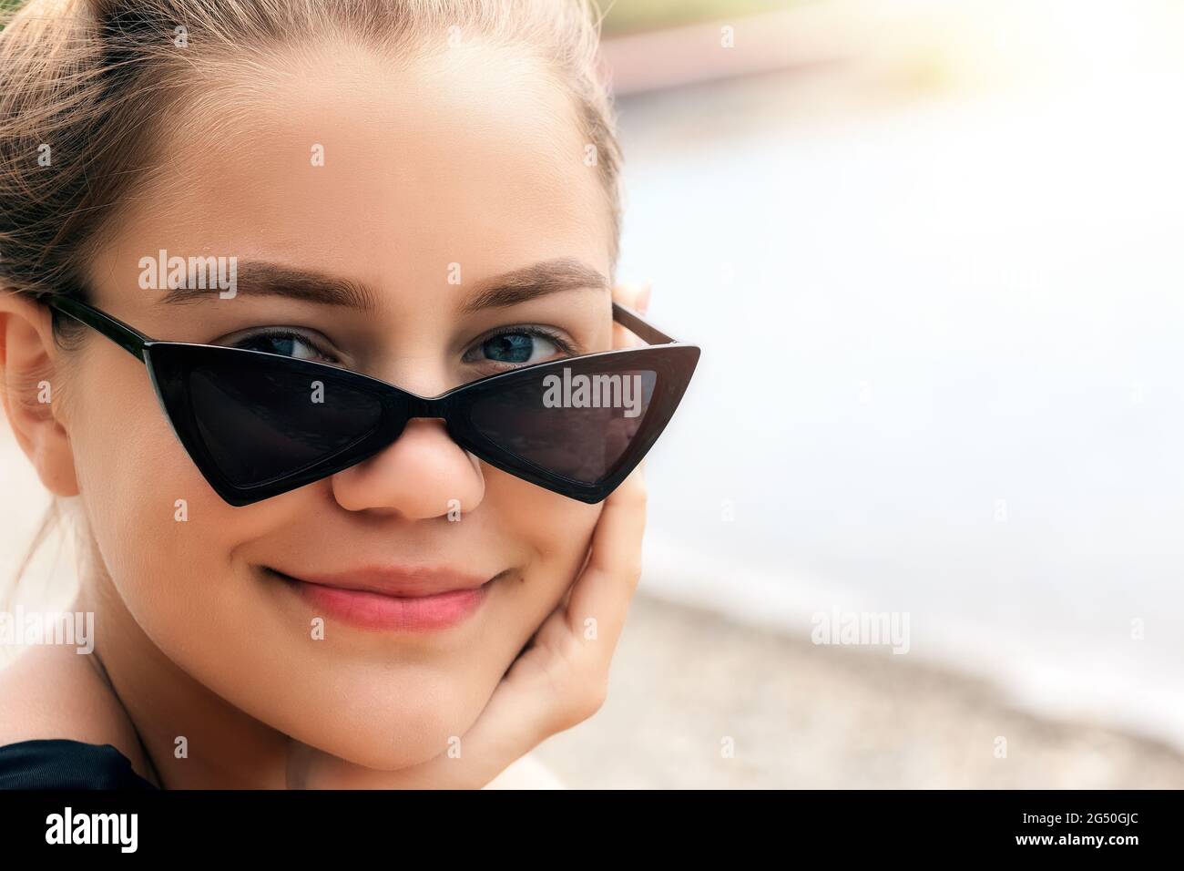 Portrait of a beautiful girl in darkened sunglasses. The look of a young Caucasian beauty from under glasses and a smile. The concept of summer rest and relaxation Stock Photo