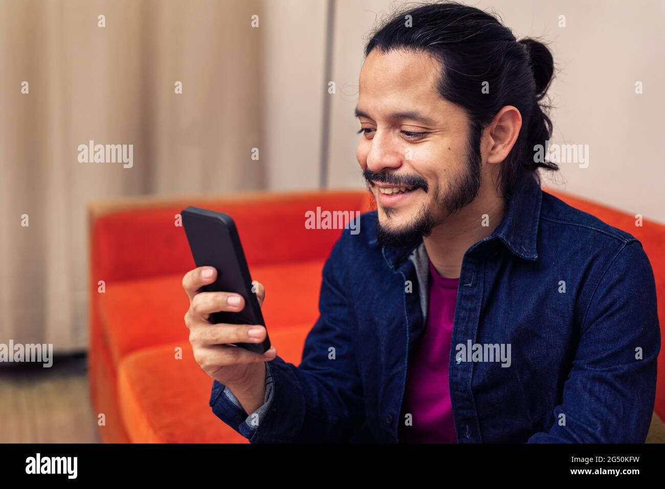 Young latin man using the phone at home in the living room at night Stock Photo