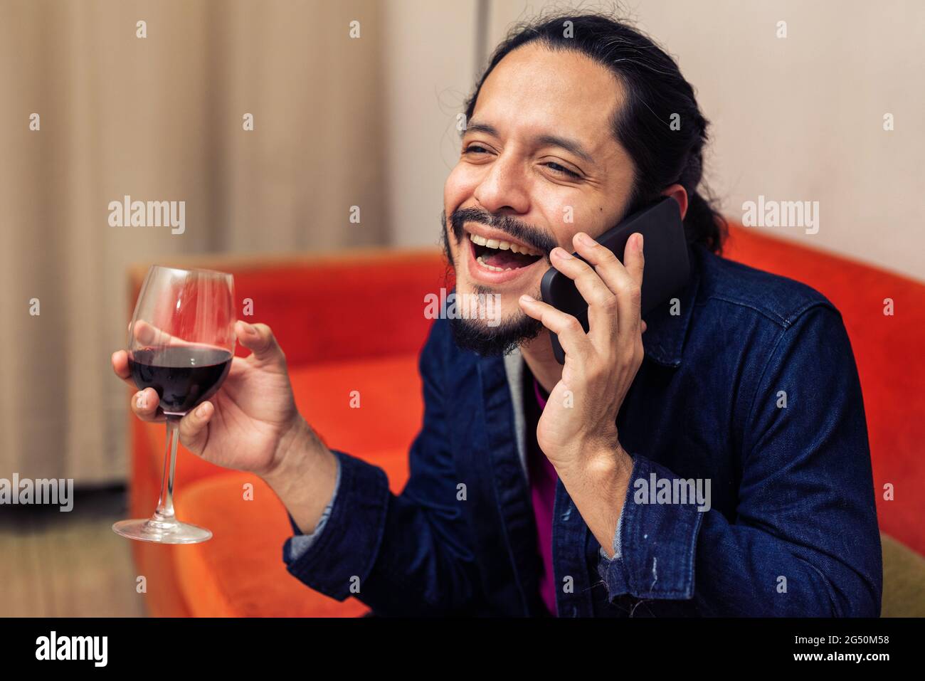 Young latin man drinking red wine at home in the living room Stock Photo