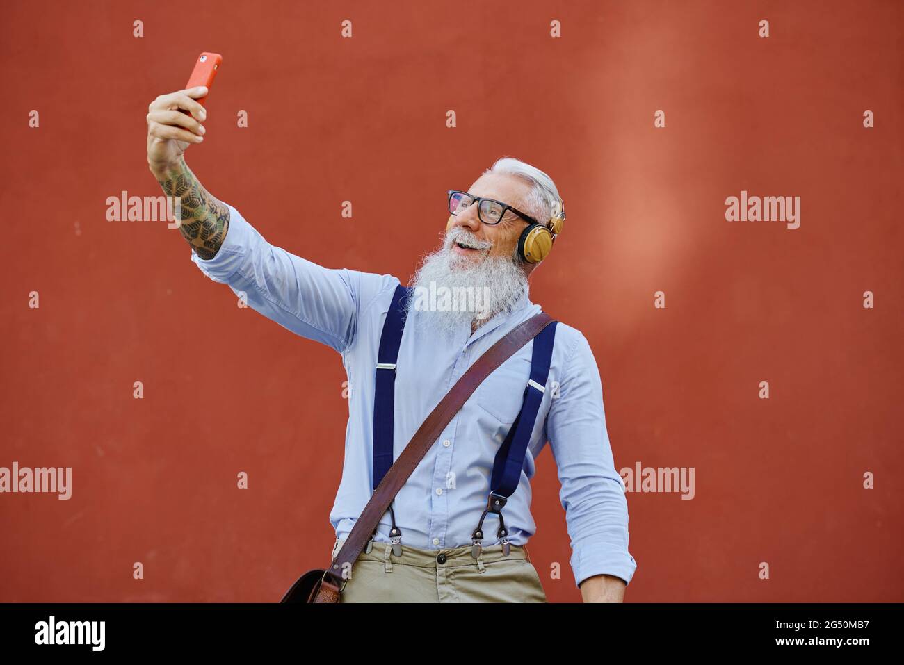 Smiling elderly man taking selfie on smartphone on red background Stock Photo