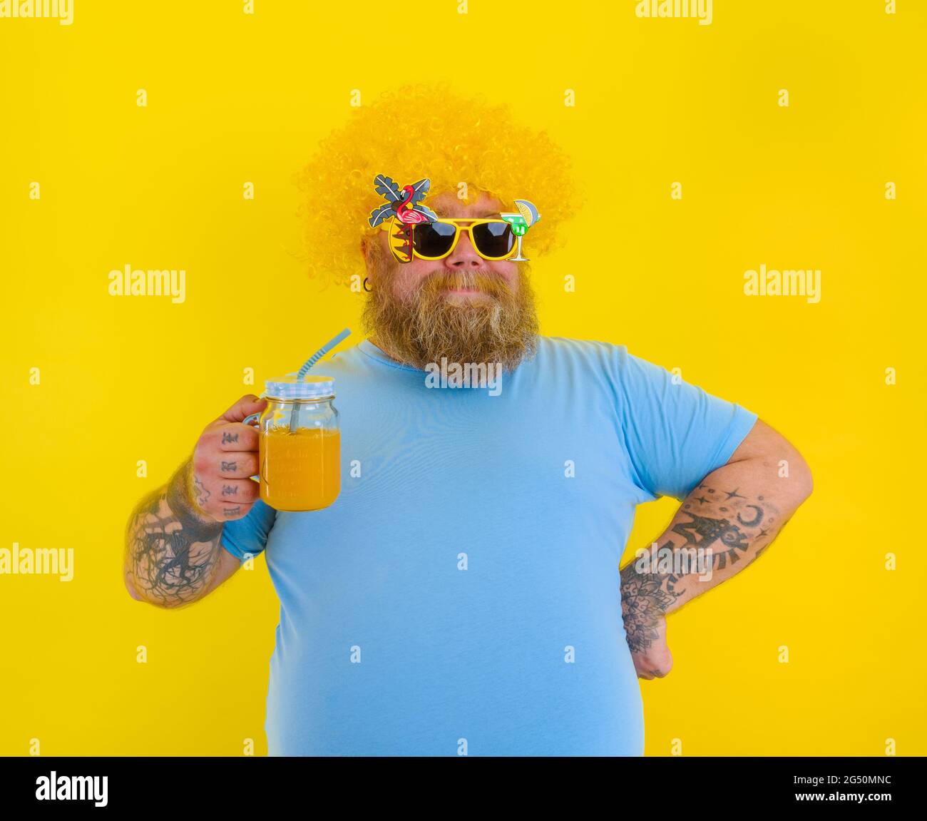 Fat happy man with wig in head and sunglasses drinks a fruit juice Stock Photo