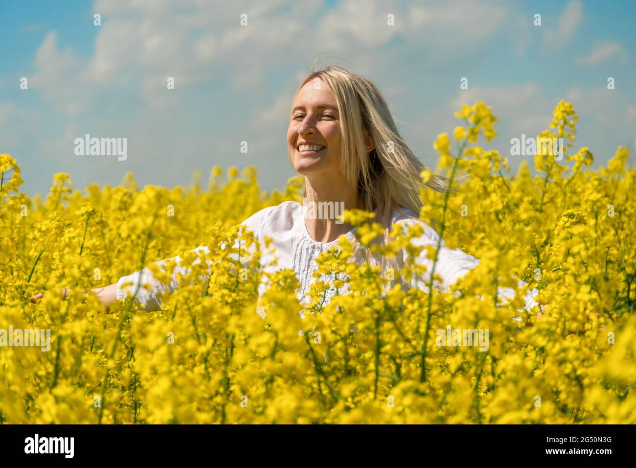 Happy smiling young blonde woman in a white shirt in a rapeseed field ...