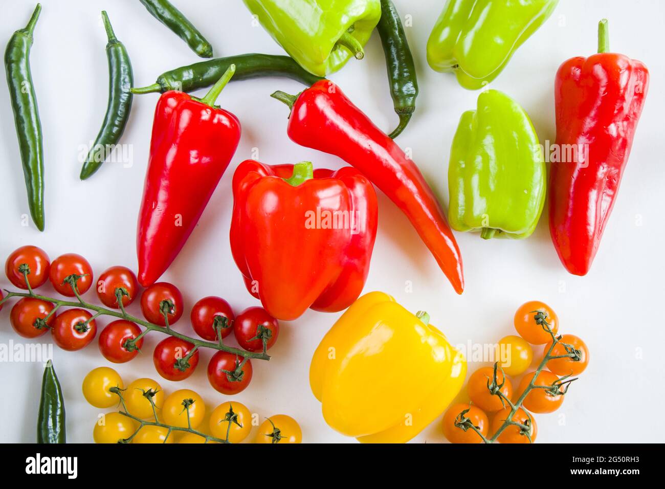 Top view of colorful bell peppers, green spicy peppers, and cherry tomatoes on a white background Stock Photo