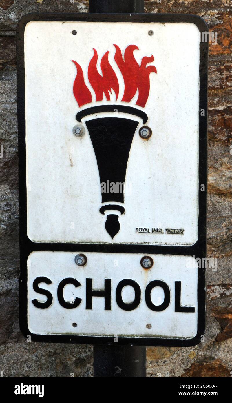A roadside sign warning drivers that there is a school ahead. The sign features The Flaming Torch of Knowledge and dates from the 1950s and 60s. Stock Photo