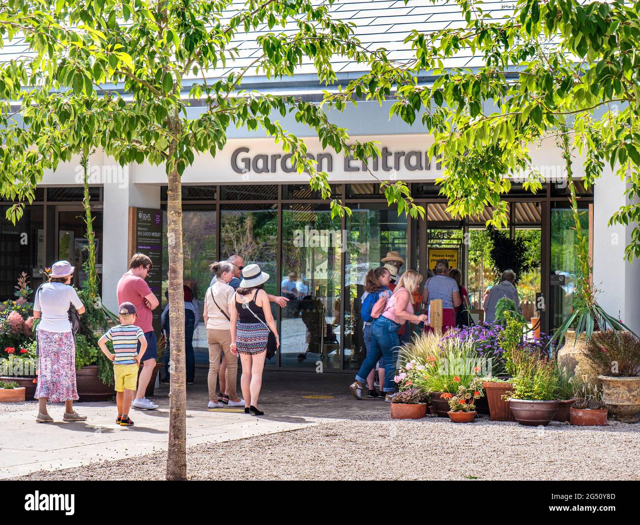 RHS Wisley Gardens entrance & socially distanced visitors waiting at the sunlit modern new entrance vestibule & Cherry Trees. Wisley Gardens Surrey UK Stock Photo