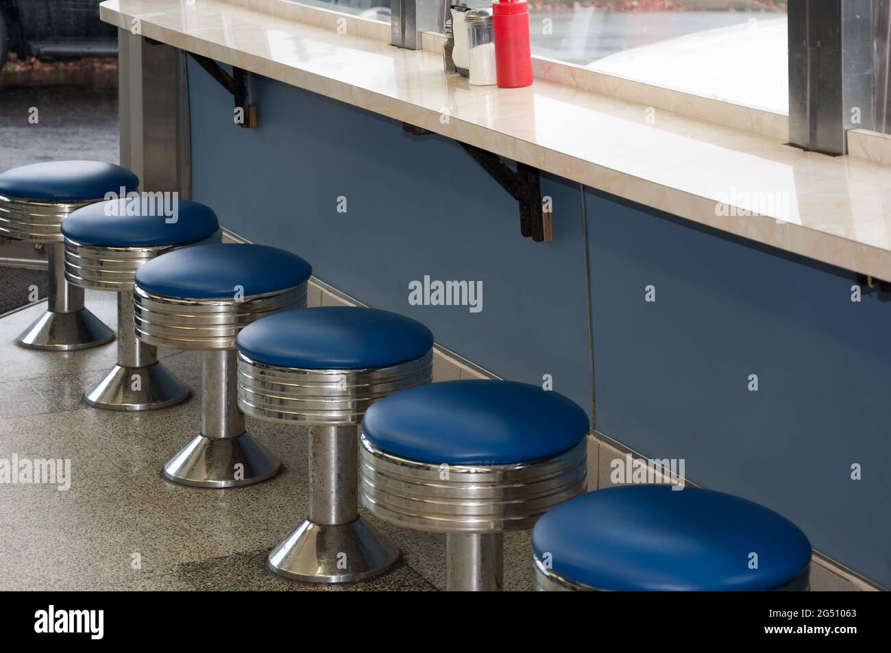 Vintage diner stools inside an old diner from the 1950's with blue vinyl seats. Stock Photo