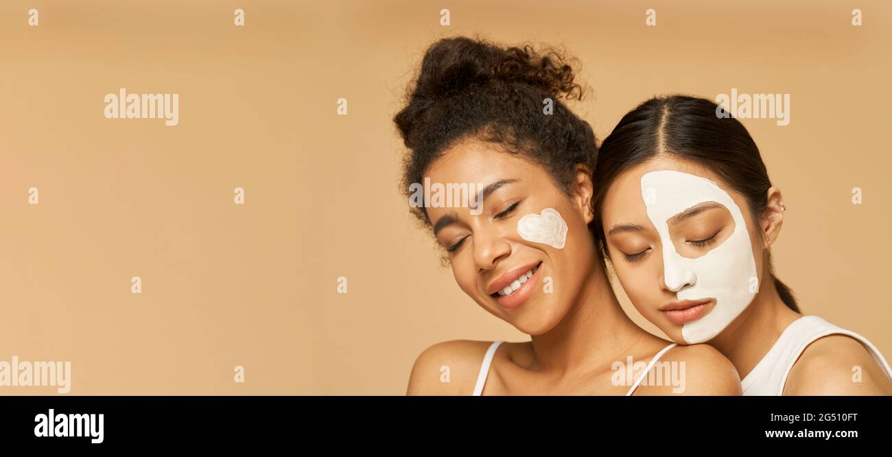 Website header of Close up portrait of two young female friends with facial masks on posing with eyes closed isolated over beige background Stock Photo