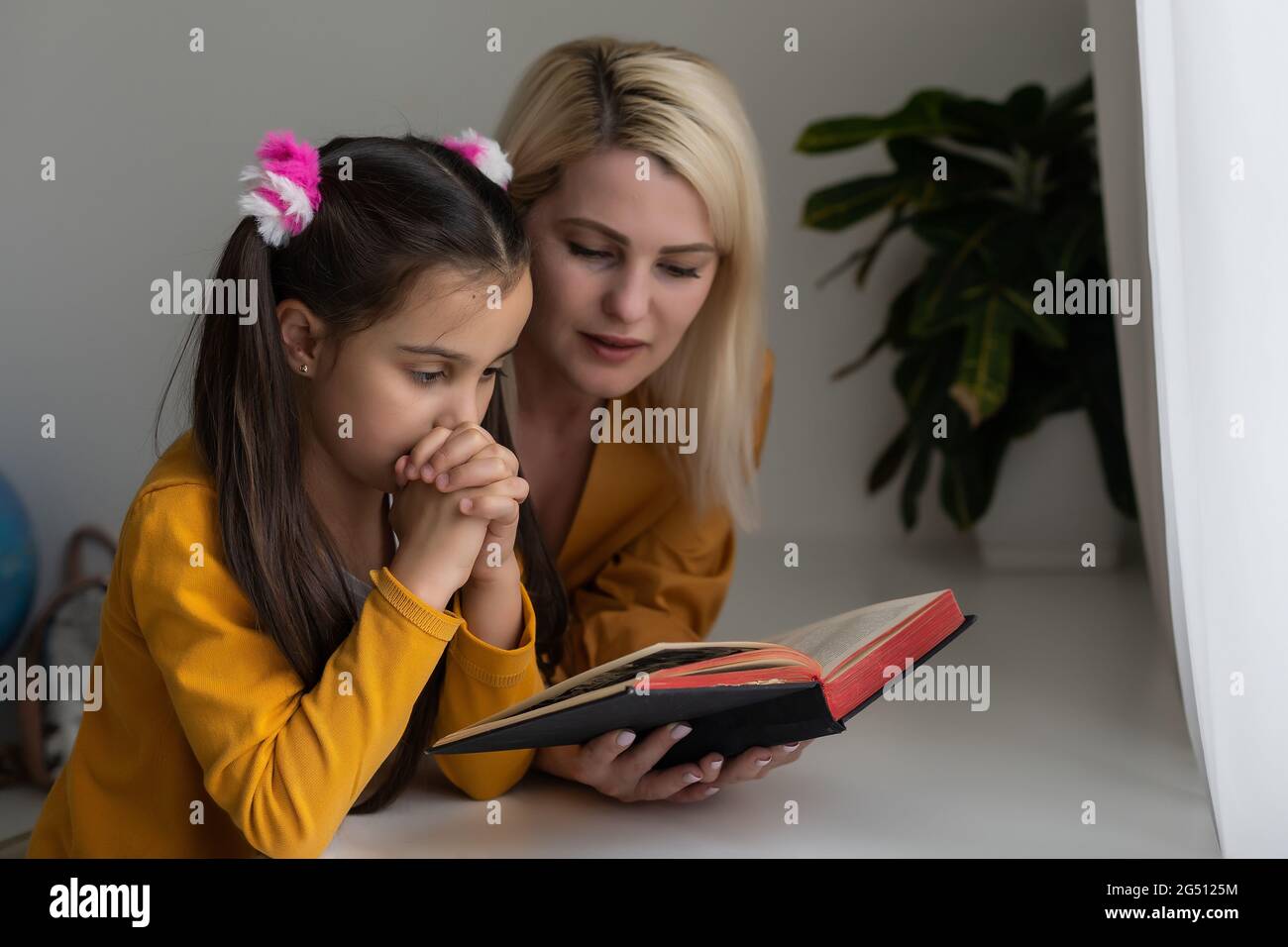 Mother and daughter reading from the bible and praying Stock Photo
