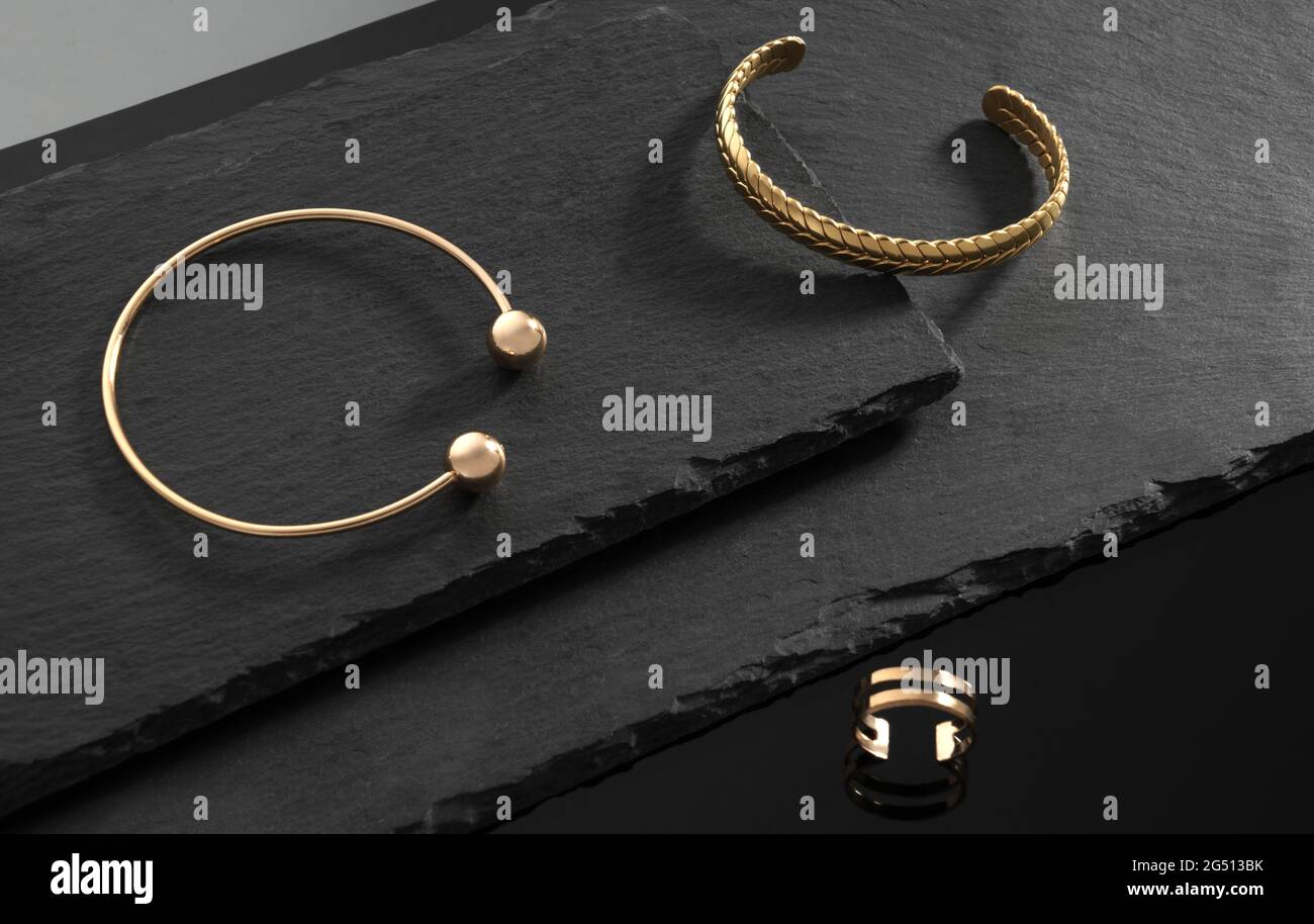 Modern design golden hand cuffs and ring on dark stone plates on black background Stock Photo