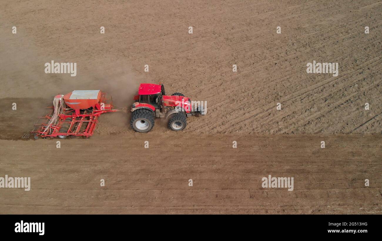 Tractor with a unit processes dusty soil on the prairie. Farmer sows in arid, lifeless steppes. Concept of risky agribusiness. Aerial side view Stock Photo